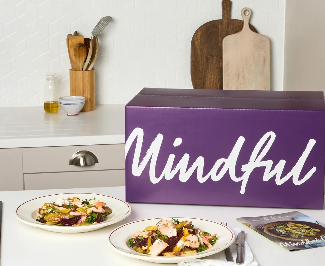 A Mindful Chef recipe box on a kitchen counter beside freshly cooked dishes